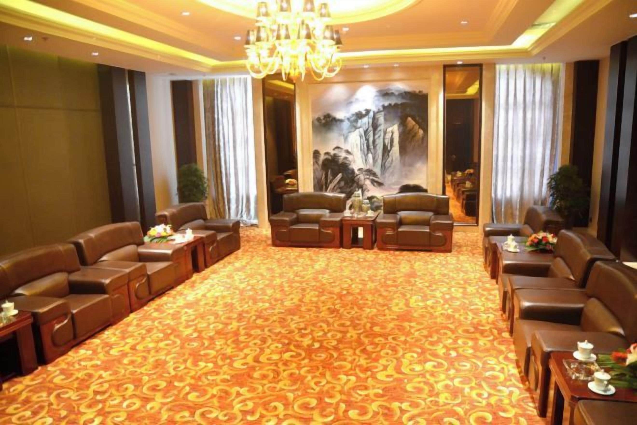 A hotel lobby with leather sofas, a carpeted floor, a chandelier, and a mural.