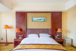 A hotel room with a bed, two bedside tables, a nightstand, a lamp, a small heater, and a painting on the wall. - Hengshui Taihua Boyue Hotel (Hengshui)