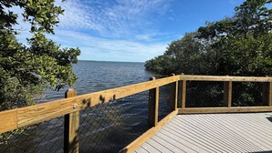 A wooden deck with a chain-link fence overlooking calm water, surrounded by dense foliage. - Charming Longboat Key Bungalow minutes from beaches, restaurants, parks (Longboat Key)