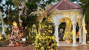 A Christmas tree adorned with lights and ornaments in a garden setting with a gazebo in the background. - Charming Longboat Key Bungalow minutes from beaches, restaurants, parks (Longboat Key)