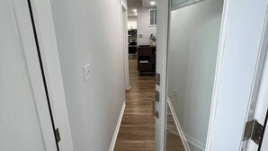 A hallway with white walls and wooden flooring leading to a kitchen area.