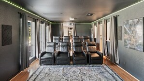A home theater room with multiple black leather recliners, a patterned rug, and a ceiling light. - Pool*Sauna*HotTub*Theater*Bar*Pickleball*Volleyball (Oakhurst)