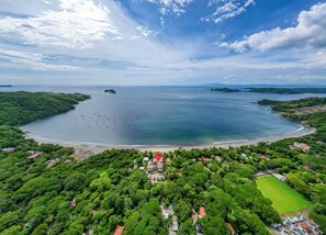 Vista aérea de uma área costeira com um extenso corpo d'água, uma praia e vegetação ao redor.