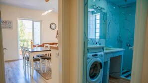 Une cuisine moderne équipée d’un lave-linge, un coin repas avec une table et des chaises, et une vue sur l’extérieur.