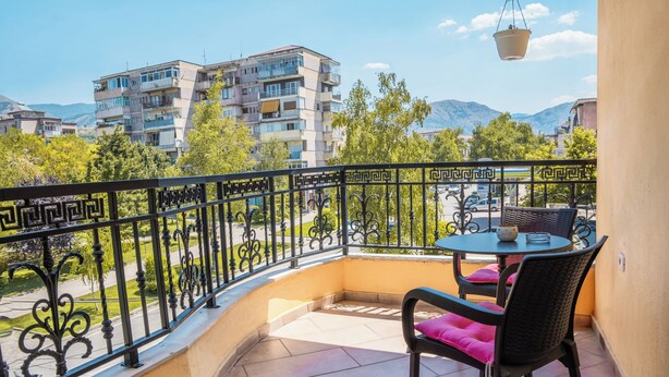 Un balcon avec une table et des chaises, un pot suspendu et une vue sur des immeubles et des arbres.