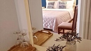 Une chambre à coucher avec un lit, une table de chevet en bois, un miroir et un vase contenant des fleurs séchées.
