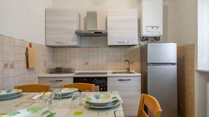 Una cucina con mobili bianchi, un frigorifero in acciaio inossidabile e un tavolo da pranzo apparecchiato con piatti e bicchieri.