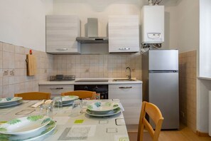 A kitchen with white cabinets, a stainless steel refrigerator, and a dining table set with plates and glasses.