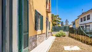 Un viuzza stretta con un sentiero lastricato, un piccolo giardino e un edificio con persiane verdi e una base in pietra.