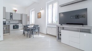 Une cuisine moderne avec des meubles blancs, un coin repas comprenant une table et des chaises, et un grand téléviseur à écran plat fixé au mur.