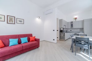 Una sala moderna con un sofá rojo, un comedor con mesa y sillas, y una cocina con armarios y electrodomésticos.