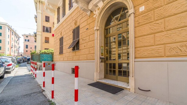 Un bâtiment doté d’une grande entrée en arc de cercle, d’une allée bordée de portails et de voitures garées le long de la rue.