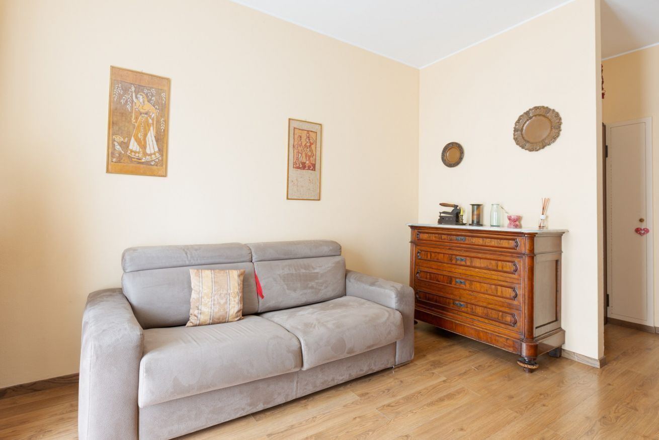 Ein Wohnzimmer mit grauem Sofa, einem Holzschrank und zwei gerahmten Bildern an der Wand.