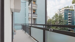 Ein Balkon mit Metallgeländer, gefliestem Boden und Blick auf ein blaues Gebäude mit Balkonen.