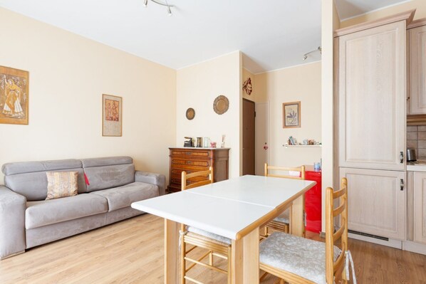 Un salon comprenant un canapé, une table à manger et des chaises. Il y a également un coin cuisine avec des placards et un réfrigérateur.