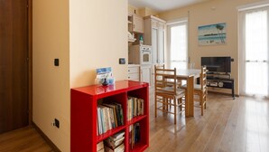 Eine Küche mit weißen Schränken, einem roten Bücherregal, einem Esstisch mit Stühlen und einem Bild an der Wand.