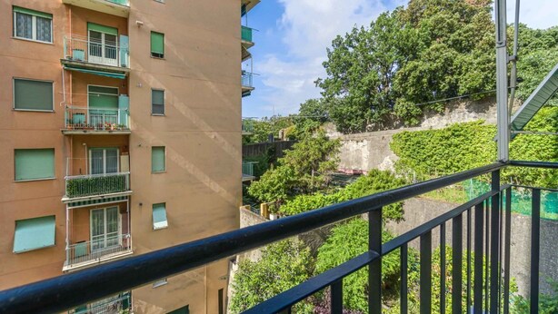 Un edificio de varios pisos con balcones, cielo despejado y vegetación al fondo.