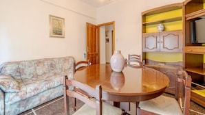 Un comedor con una mesa redonda, sillas, un jarrón, un sofá y un aparador con estantes.