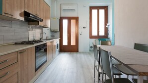 A kitchen with wooden cabinets, a stove, a washing machine, and a dining area with a table and chairs. - GuestHost - Turquoise Mini Flat x2 near Centrale FS (Milan)