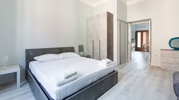 A modern bedroom with a large bed, a bedside table, a wardrobe, and a bathroom visible through an open door. - GuestHost - Turquoise Mini Flat x2 near Centrale FS (Milan)