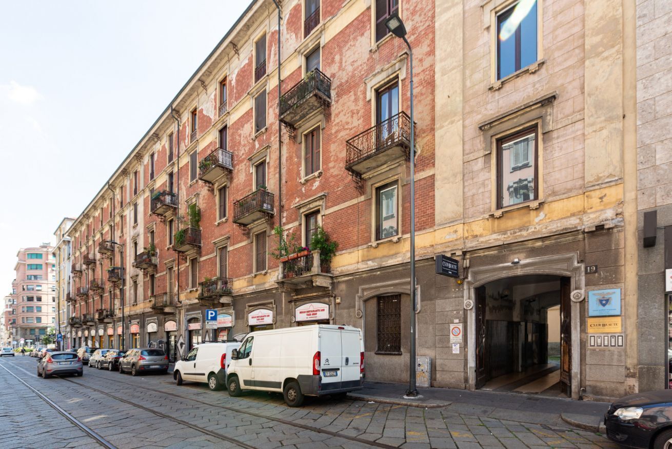 A row of multi-story buildings with balconies, a tram line, and parked vehicles.