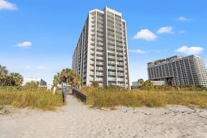 A beachfront hotel with a central tower and a smaller adjacent building, featuring a sandy walkway leading to the entrance. - 2BR/2BA Oceanview Condo at Kingston Resort (Myrtle Beach)