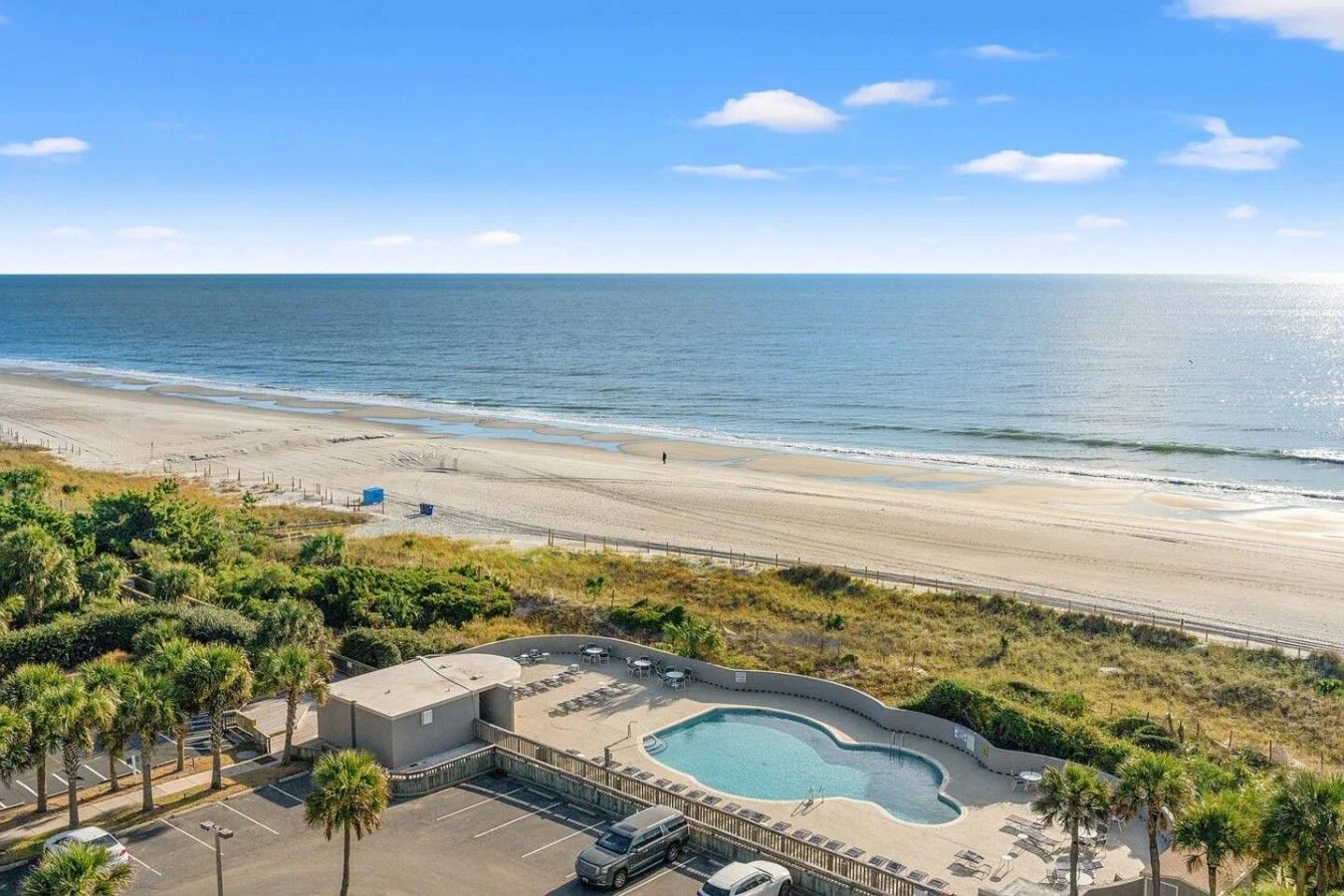 A beachfront property with a swimming pool, parking area, and a view of the ocean.