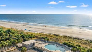 A beachfront property with a swimming pool, parking area, and a view of the ocean.