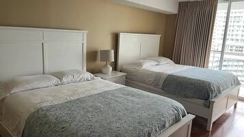 A hotel room with two beds, a nightstand with a lamp, and a large window with curtains.