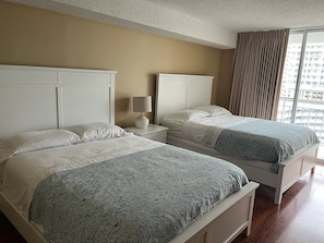 A hotel room with two beds, a nightstand with a lamp, and a large window with curtains. - 2BR/2BA Oceanview Condo at Kingston Resort (Myrtle Beach)