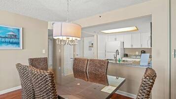A dining area with a table and chairs, a hanging light fixture, and a view into the kitchen area.