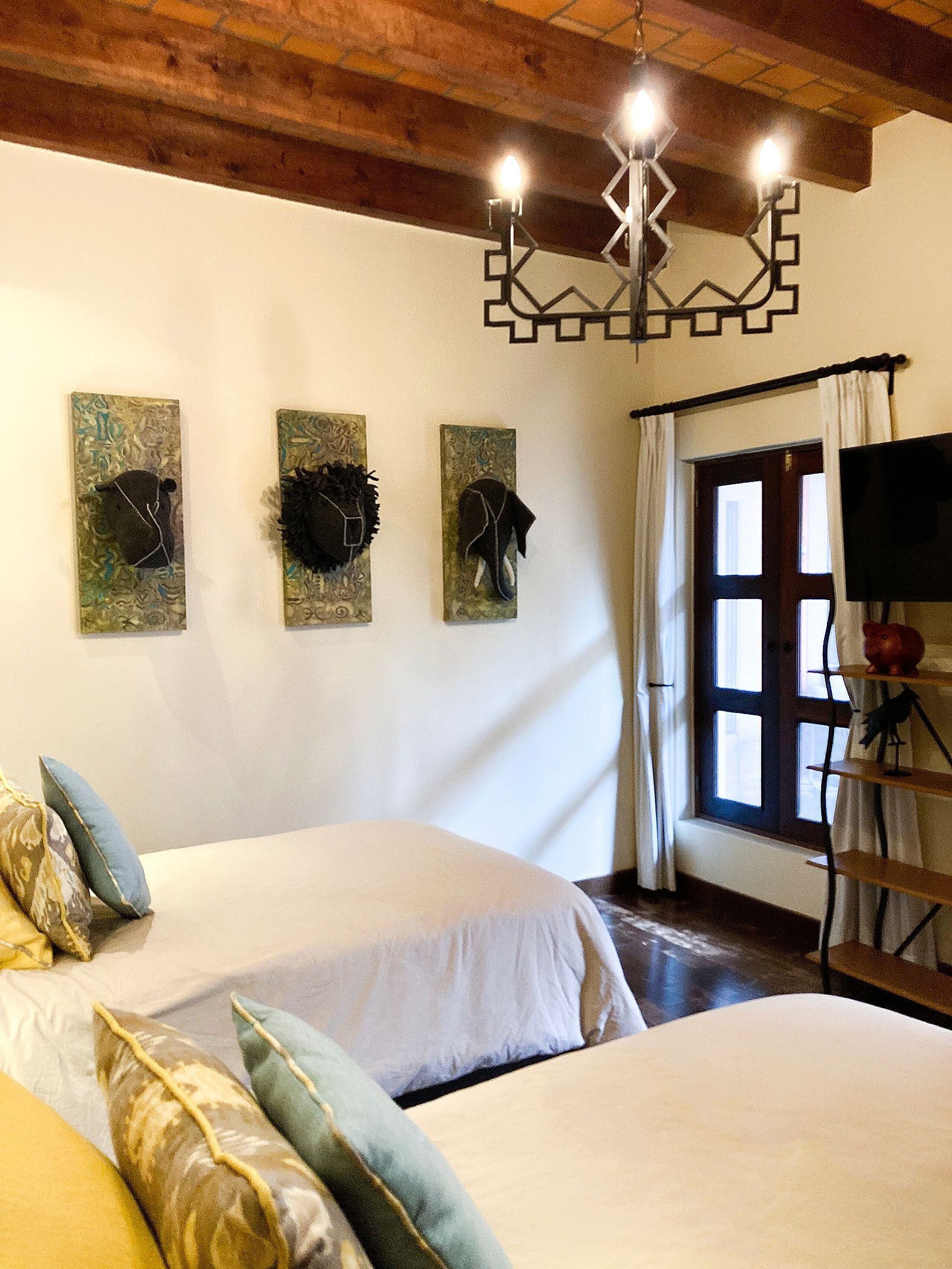 A room with two beds, a wooden ceiling, a chandelier, and artwork on the wall.