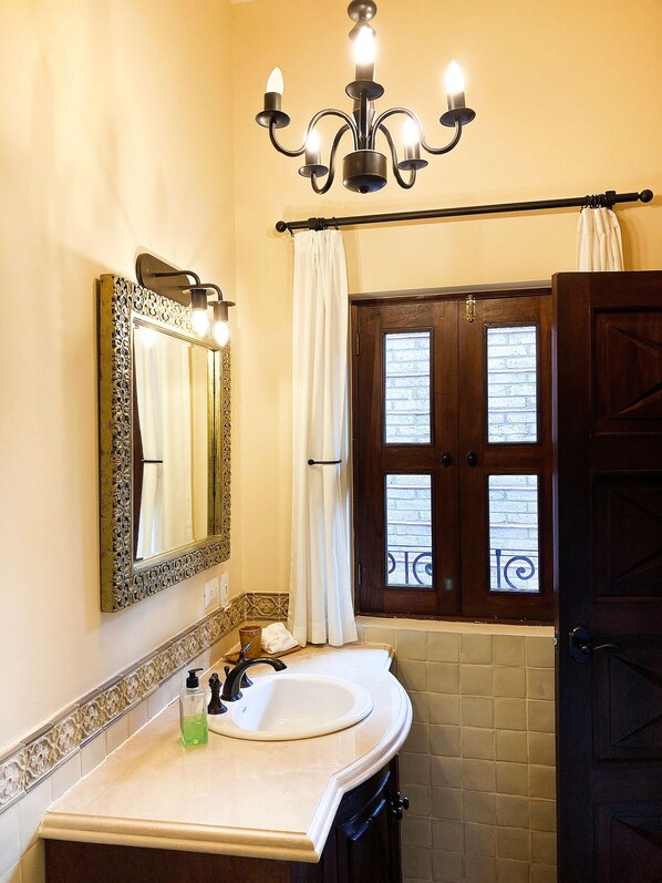 A bathroom with a large mirror, a chandelier, a sink, and a door with a window.
