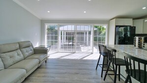 A spacious living room with a beige sofa, a dining area with bar stools, and a kitchen with a refrigerator. - 4 Bd 4 Ba w/ Private Studio 10 G WIFI and AC (Hayward)