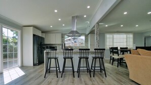 A modern kitchen with a central island, bar stools, and a dining area with a sofa. - 4 Bd 4 Ba w/ Private Studio 10 G WIFI and AC (Hayward)