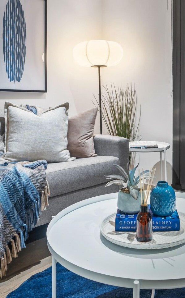 A modern living room with a grey sofa, a round coffee table with decorative items, a floor lamp, and a framed abstract artwork on the wall.
