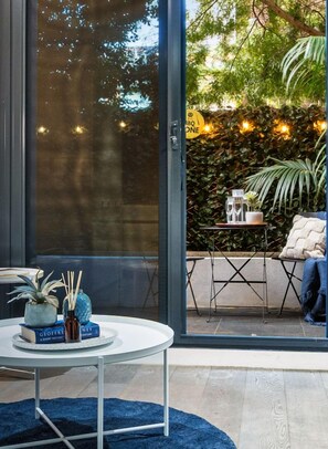 A modern room with a large glass door leading to an outdoor area with a table set for two, a potted plant, and a cozy seating area.