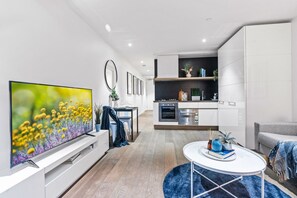 A modern living room with a flat-screen TV, a dining area, a kitchen, and a grey sofa. - Elwood Beachside Escape (Elwood)