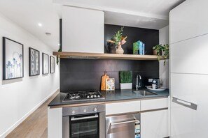 A modern kitchen with a gas stove, oven, and built-in dishwasher. There is a wooden shelf with decorative items and a potted plant.
