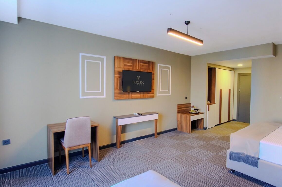 Une chambre d’hôtel comprenant un lit, un bureau, une chaise, un téléviseur fixé au mur et une porte donnant sur une autre pièce.