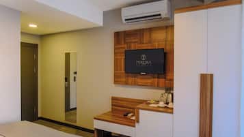 Una habitación de hotel con una cama, un tocador de madera con espejo, un televisor montado en la pared y un equipo de aire acondicionado.