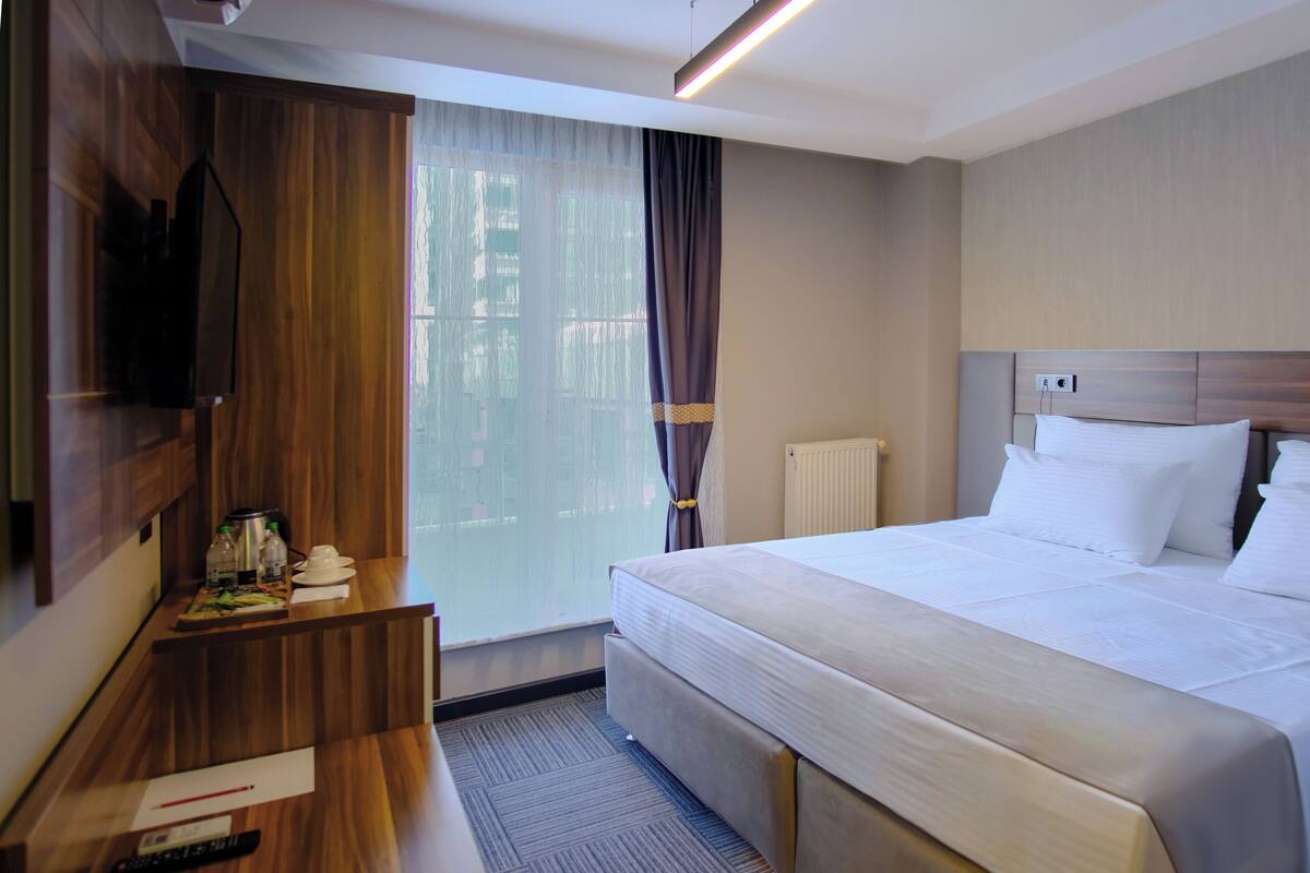 A hotel room with a large bed, a desk with a flat-screen TV, a coffee maker, and a window with curtains.