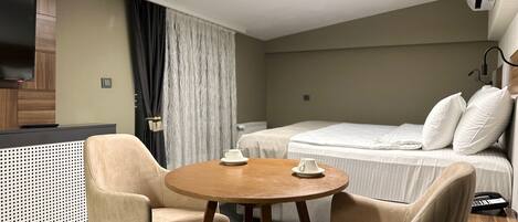Habitación de hotel con cama, dos sillones, una mesita redonda, televisor y minibar.