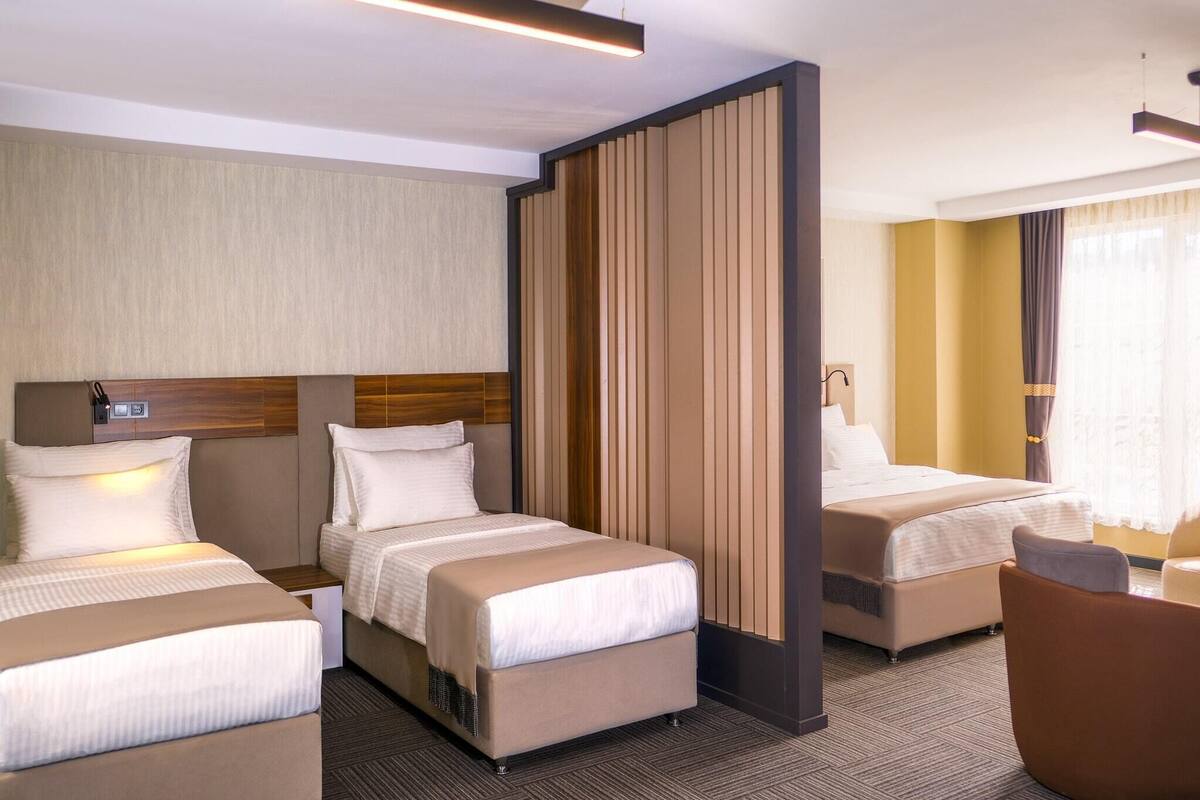 A hotel room with two beds, a wooden partition, a chair, and a bedside table.