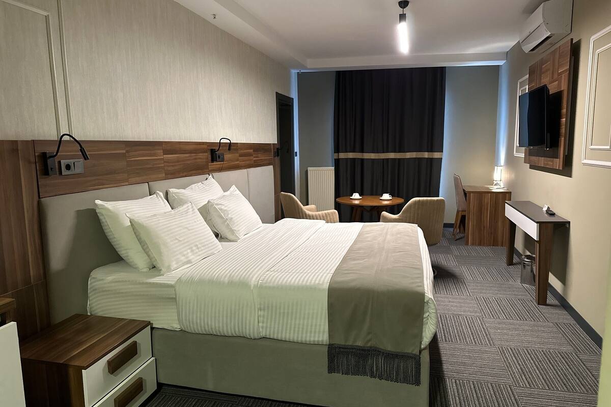 A hotel room with a large bed, a desk, a chair, a TV, and a window with curtains.