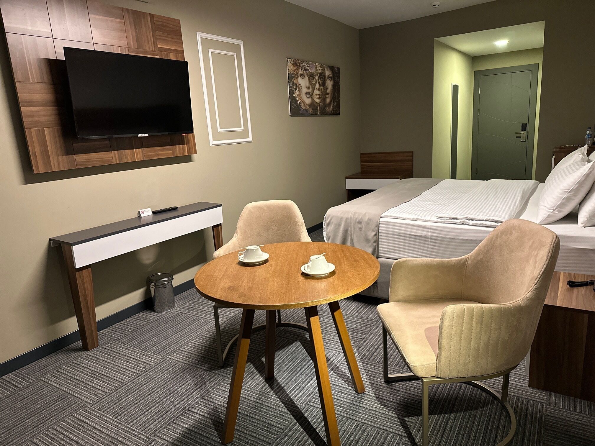A hotel room with a bed, a desk, a TV, and two chairs.