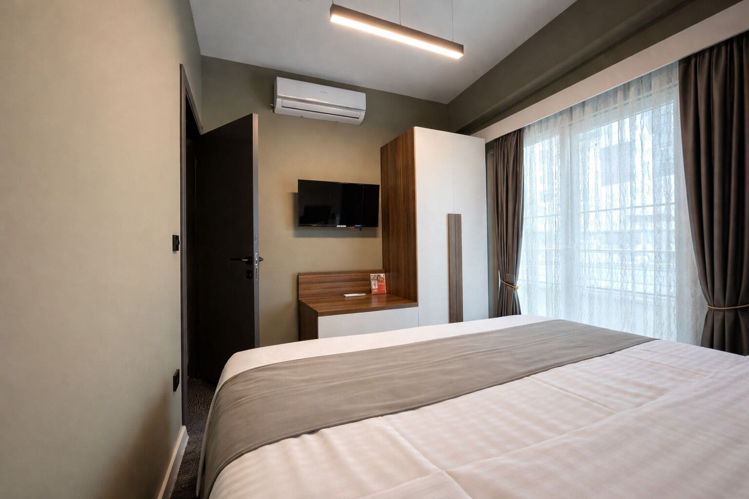 Una habitación de hotel con cama, televisión, escritorio y ventana con cortinas.