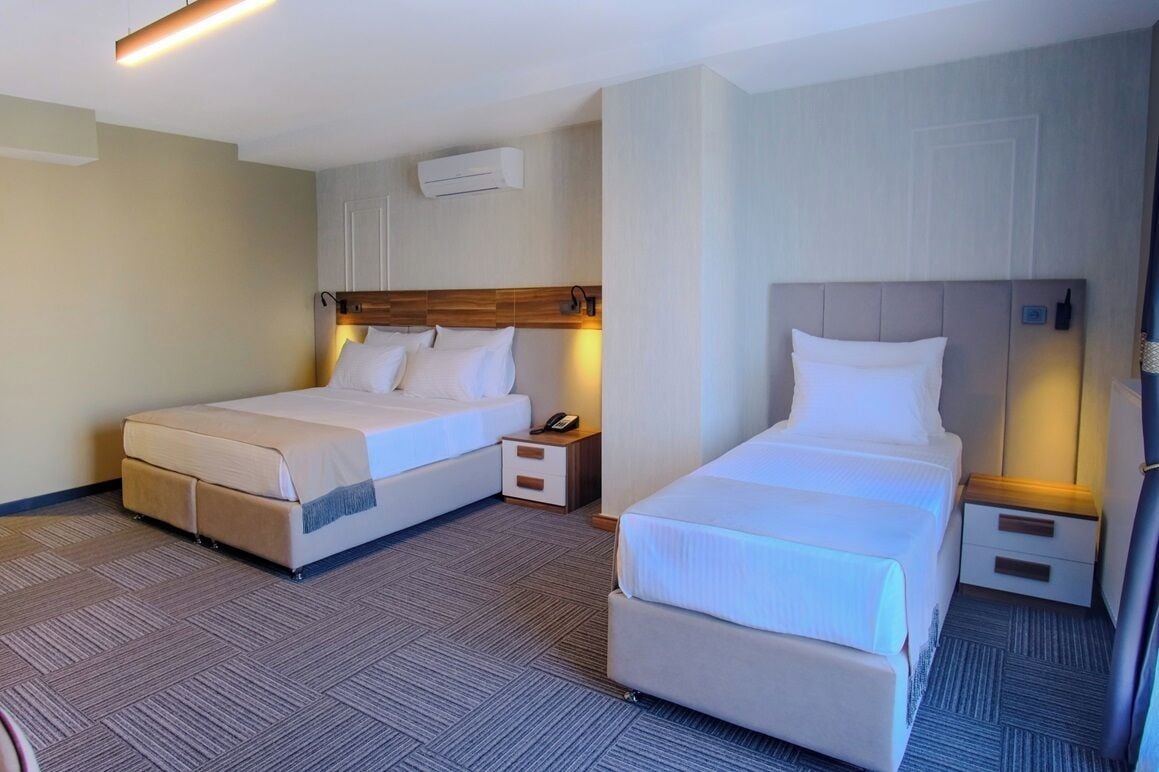 Quarto de hotel com duas camas, cabeceira de madeira, mesas de cabeceira e ar condicionado.