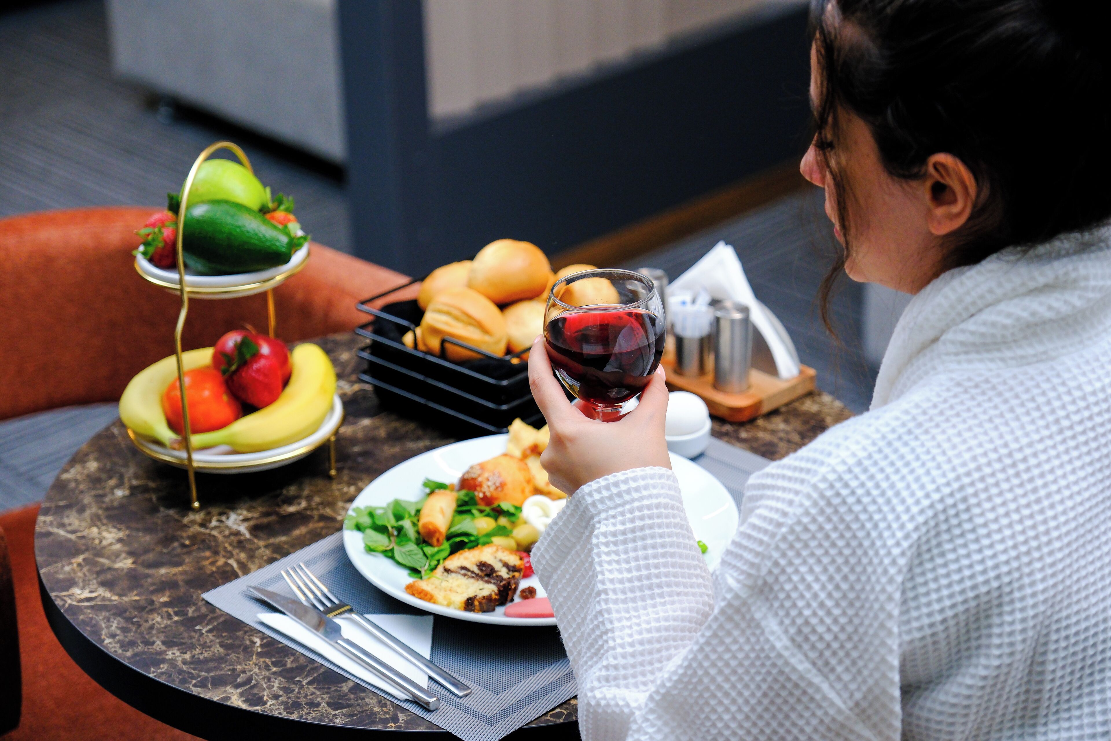 A dining table with a plate of food, a glass of red wine, and a fruit basket.