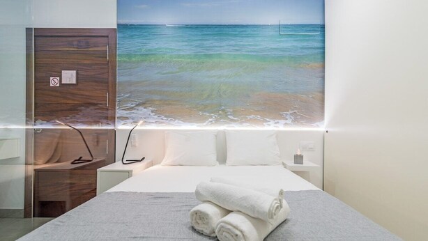 A hotel room with a bed, a nightstand, a lamp, and a wall with a beach view.